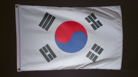 Studio-Shot-Of-Flag-Of-South-Korea-Falling-Down-Against-Black-Background