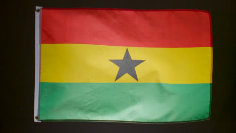 Studio-Shot-Of-Flag-Of-Ghana-Flying-Against-Black-Background