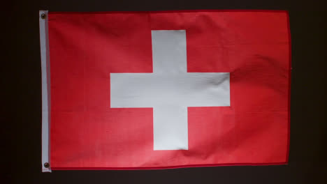 Studioaufnahme-Der-Flagge-Der-Schweiz-Vor-Schwarzem-Hintergrund