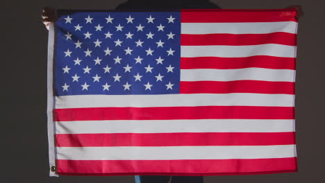 Studio-Shot-Of-Anonymous-Person-Or-Sports-Fan-Holding-Flag-Of-America-Against-Black-Background