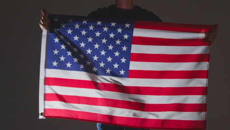 Studio-Shot-Of-Anonymous-Person-Or-Sports-Fan-Waving-Flag-Of-America-Against-Black-Background