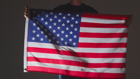 Foto-De-Estudio-De-Una-Persona-Anónima-O-Fanático-De-Los-Deportes-Ondeando-La-Bandera-De-América-Contra-El-Fondo-Negro