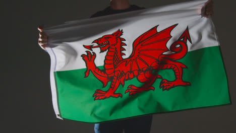 Studio-Shot-Of-Anonymous-Person-Or-Sports-Fan-Waving-Flag-Of-Wales-Against-Black-Background