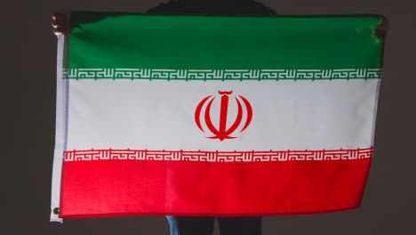 Studio-Shot-Of-Anonymous-Person-Or-Sports-Fan-Holding-Flag-Of-Iran-Against-Black-Background