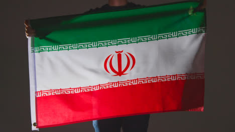 Studioaufnahme-Einer-Anonymen-Person-Oder-Eines-Sportfans,-Die-Die-Flagge-Des-Iran-Vor-Schwarzem-Hintergrund-Schwenken