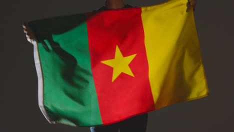 Studioaufnahme-Einer-Anonymen-Person-Oder-Eines-Sportfans,-Der-Die-Flagge-Kameruns-Vor-Schwarzem-Hintergrund-Schwenkt
