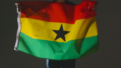 Foto-De-Estudio-De-Una-Persona-Anónima-O-Fanático-De-Los-Deportes-Ondeando-La-Bandera-De-Ghana-Contra-Fondo-Negro