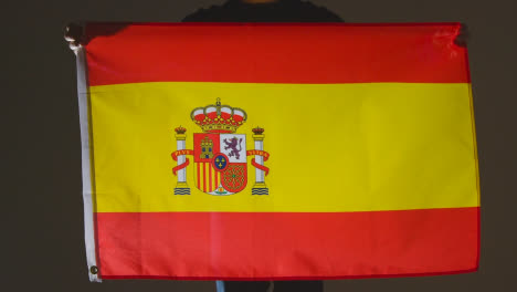 Studio-Shot-Of-Anonymous-Person-Or-Sports-Fan-Holding-Flag-Of-Spain-Against-Black-Background