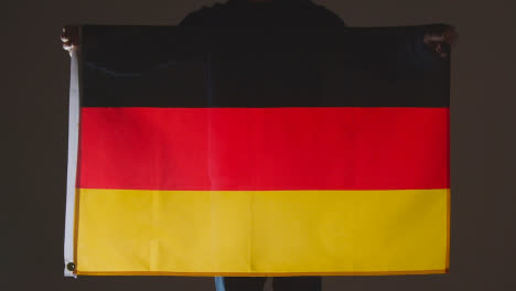 Studio-Shot-Of-Anonymous-Person-Or-Sports-Fan-Holding-Flag-Of-Germany-Against-Black-Background