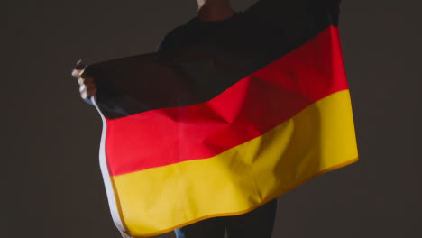 Foto-De-Estudio-De-Una-Persona-Anónima-O-Fanático-De-Los-Deportes-Ondeando-La-Bandera-De-Alemania-Contra-Fondo-Negro