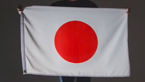 Studio-Shot-Of-Anonymous-Person-Or-Sports-Fan-Holding-Flag-Of-Japan-Against-Black-Background
