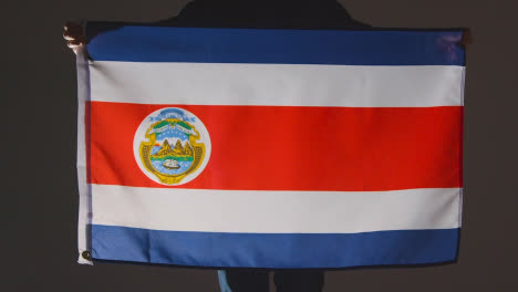 Studio-Shot-Of-Anonymous-Person-Or-Sports-Fan-Holding-Flag-Of-Costa-Rica-Against-Black-Background