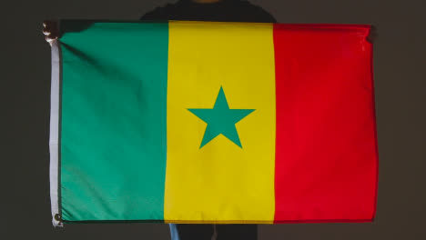 Foto-De-Estudio-De-Una-Persona-Anónima-O-Fanático-De-Los-Deportes-Que-Sostiene-La-Bandera-De-Senegal-Contra-Fondo-Negro
