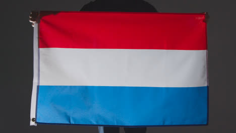 Studio-Shot-Of-Anonymous-Person-Or-Sports-Fan-Holding-Flag-Of-Netherlands-Against-Black-Background