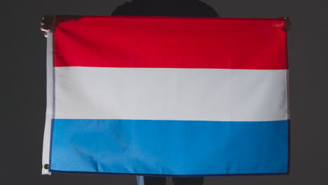 Studioaufnahme-Einer-Anonymen-Person-Oder-Eines-Sportfans,-Der-Die-Flagge-Der-Niederlande-Vor-Schwarzem-Hintergrund-Hält