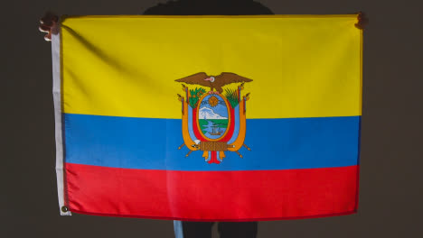 Studio-Shot-Of-Anonymous-Person-Or-Sports-Fan-Holding-Flag-Of-Ecuador-Against-Black-Background
