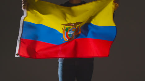 Studioaufnahme-Einer-Anonymen-Person-Oder-Eines-Sportfans,-Die-Die-Flagge-Ecuadors-Vor-Schwarzem-Hintergrund-Schwenken