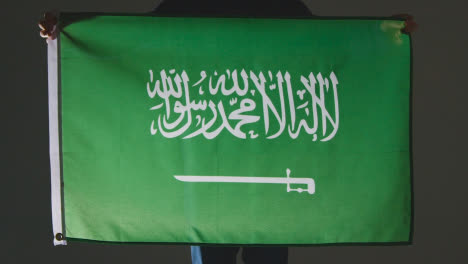 Studioaufnahme-Einer-Anonymen-Person-Oder-Eines-Sportfans,-Der-Die-Flagge-Von-Saudi-arabien-Vor-Schwarzem-Hintergrund-Hält