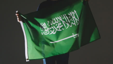 Studioaufnahme-Einer-Anonymen-Person-Oder-Eines-Sportfans,-Die-Die-Flagge-Saudi-arabiens-Vor-Schwarzem-Hintergrund-Schwenken