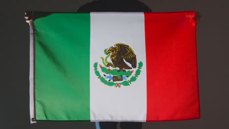 Foto-De-Estudio-De-Una-Persona-Anónima-O-Fanático-De-Los-Deportes-Sosteniendo-La-Bandera-De-México-Contra-Fondo-Negro