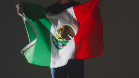 Studio-Shot-Of-Anonymous-Person-Or-Sports-Fan-Waving-Flag-Of-Mexico-Against-Black-Background