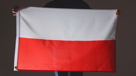 Studio-Shot-Of-Anonymous-Person-Or-Sports-Fan-Holding-Flag-Of-Poland-Against-Black-Background
