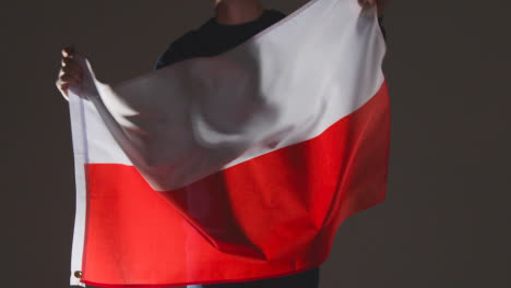 Studio-Shot-Of-Anonymous-Person-Or-Sports-Fan-Waving-Flag-Of-Poland-Against-Black-Background