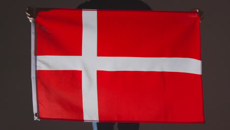 Studio-Shot-Of-Anonymous-Person-Or-Sports-Fan-Holding-Flag-Of-Denmark-Against-Black-Background