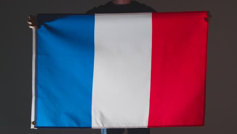 Studio-Shot-Of-Anonymous-Person-Or-Sports-Fan-Holding-Flag-Of-France-Against-Black-Background