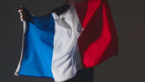 Studio-Shot-Of-Anonymous-Person-Or-Sports-Fan-Waving-Flag-Of-France-Against-Black-Background
