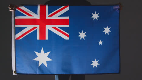 Studio-Shot-Of-Anonymous-Person-Or-Sports-Fan-Holding-Flag-Of-Australia-Against-Black-Background