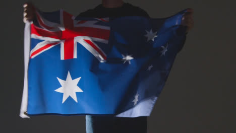 Studio-Shot-Of-Anonymous-Person-Or-Sports-Fan-Waving-Flag-Of-Australia-Against-Black-Background