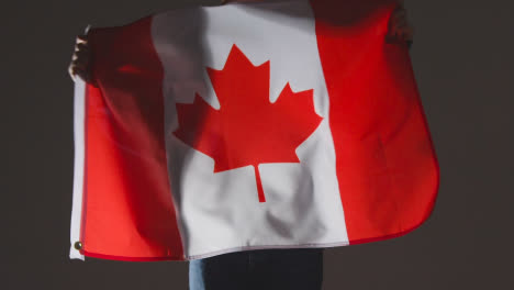 Studio-Shot-Of-Anonymous-Person-Or-Sports-Fan-Waving-Flag-Of-Canada-Against-Black-Background