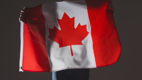 Foto-De-Estudio-De-Una-Persona-Anónima-O-Fanático-De-Los-Deportes-Ondeando-La-Bandera-De-Canadá-Contra-Fondo-Negro