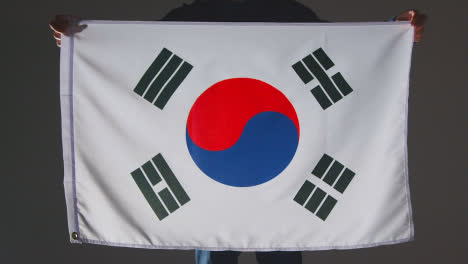 Studio-Shot-Of-Anonymous-Person-Or-Sports-Fan-Holding-Flag-Of-South-Korea-Against-Black-Background