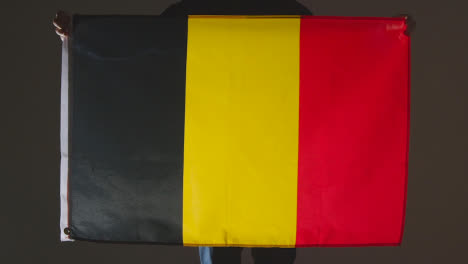 Studio-Shot-Of-Anonymous-Person-Or-Sports-Fan-Holding-Flag-Of-Belgium-Against-Black-Background