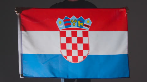 Studio-Shot-Of-Anonymous-Person-Or-Sports-Fan-Holding-Flag-Of-Croatia-Against-Black-Background