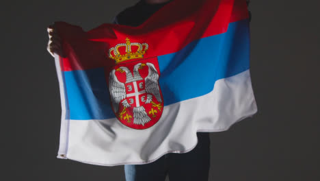 Studio-Shot-Of-Anonymous-Person-Or-Sports-Fan-Waving-Flag-Of-Serbia-Against-Black-Background