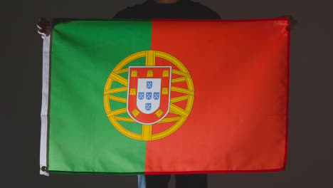 Studio-Shot-Of-Anonymous-Person-Or-Sports-Fan-Holding-Flag-Of-Portugal-Against-Black-Background