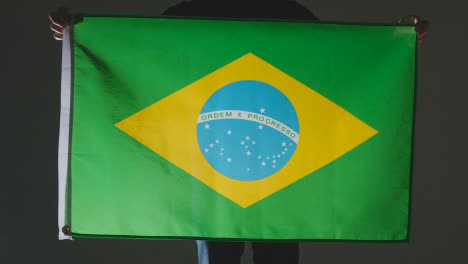 Studioaufnahme-Einer-Anonymen-Person-Oder-Eines-Sportfans,-Der-Die-Flagge-Von-Brasilien-Vor-Schwarzem-Hintergrund-Hält