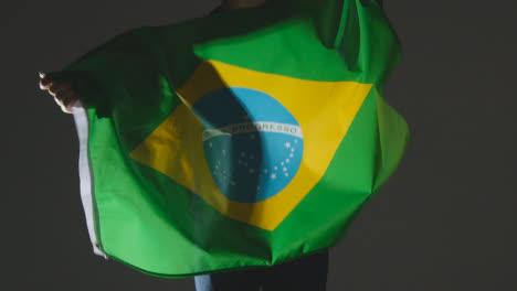 Studioaufnahme-Einer-Anonymen-Person-Oder-Eines-Sportfans,-Die-Die-Flagge-Brasiliens-Vor-Schwarzem-Hintergrund-Schwenken