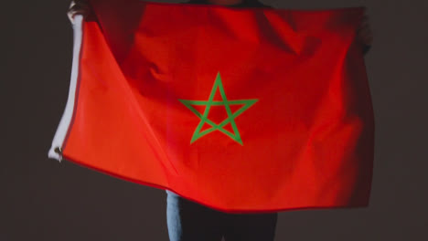 Foto-De-Estudio-De-Una-Persona-Anónima-O-Fanático-De-Los-Deportes-Ondeando-La-Bandera-De-Marruecos-Contra-El-Fondo-Negro
