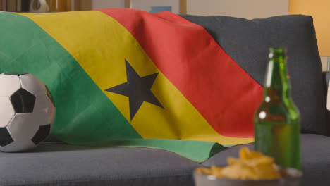 Flagge-Von-Ghana-Zu-Hause-über-Sofa-Drapiert,-Fußball-Bereit-Für-Spiel-Im-Fernsehen-2