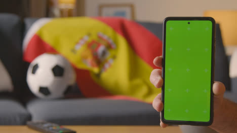 Green-Screen-Handy-Mit-Spanischer-Flagge,-Die-Zu-Hause-über-Dem-Sofa-Drapiert-Ist,-Bereit-Für-Ein-Fußballspiel