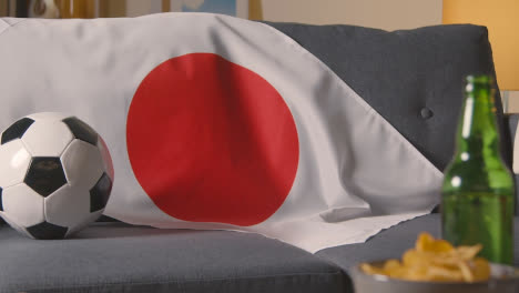 Flag-Of-Japan-Draped-Over-Sofa-At-Home-With-Football-Ready-For-Match-On-TV-1