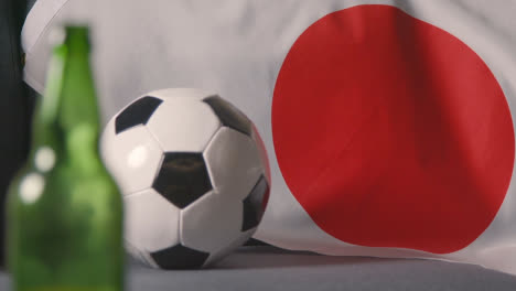 Nahaufnahme-Der-Flagge-Von-Japan,-Die-Zu-Hause-über-Dem-Sofa-Drapiert-Ist,-Mit-Dem-Fußball,-Der-Für-Das-Spiel-Im-Fernsehen-Bereit-Ist