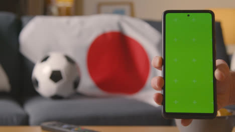 Teléfono-Móvil-De-Pantalla-Verde-Con-Bandera-Japonesa-Sobre-Un-Sofá-En-Casa-Listo-Para-El-Partido-De-Fútbol