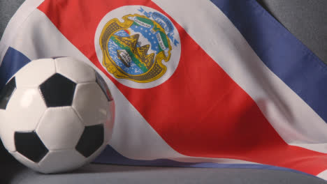 Nahaufnahme-Der-Flagge-Von-Costa-Rica,-Die-Zu-Hause-über-Dem-Sofa-Drapiert-Ist,-Mit-Dem-Fußball,-Der-Für-Das-Spiel-Im-Fernsehen-Bereit-Ist