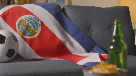 Flagge-Von-Costa-Rica-Zu-Hause-über-Sofa-Drapiert,-Fußball-Bereit-Für-Spiel-Im-Tv-2
