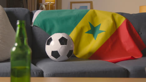 Flag-Of-Senegal-Draped-Over-Sofa-At-Home-With-Football-Ready-For-Match-On-TV